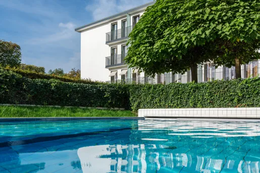 Outdoor pool with trimmed bushes and a white building in the background