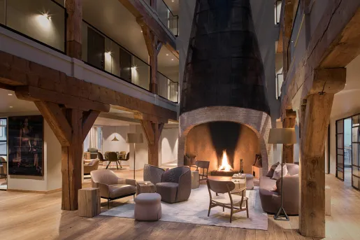 Indoor lobby and lounge with cushioned chairs in front of a large, stone fireplace