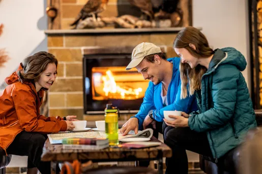 Man and two women sitting by a table in front of a fireplace, looking at a large map