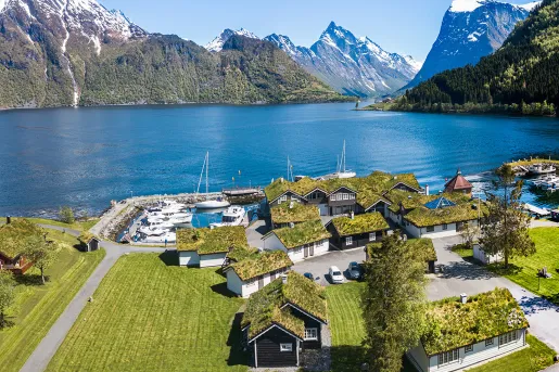 Sky view of small houses by a lake, with large mountains in the background