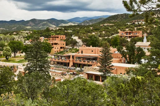 Exterior view  of orange building complex surrounded by tall trees and mountains