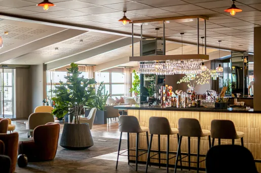Bar and lounge with cushioned stools and chairs, with a bar counter to the right