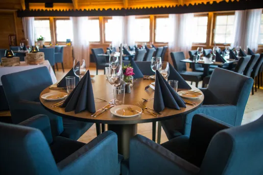 Dining hall with blue, cushioned chairs and table cloths, with wine glasses on each table