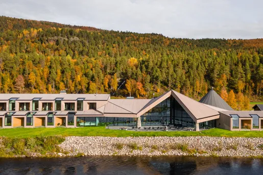Long hotel complex with large glass walls and a forest in the background