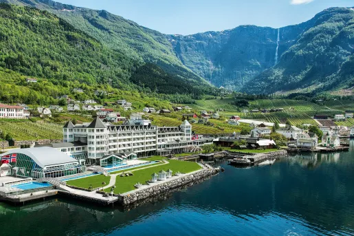 Exterior, wide view of a white hotel complex in front of a port with boats in front