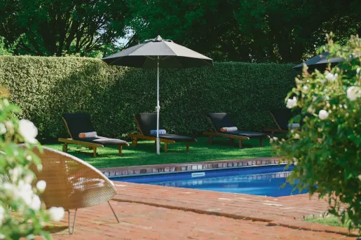 Outdoor pool surrounded by wooden chairs and trimmed hedges