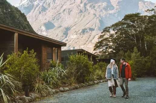 Man and woman walking along a cabin, with large mountains in the background
