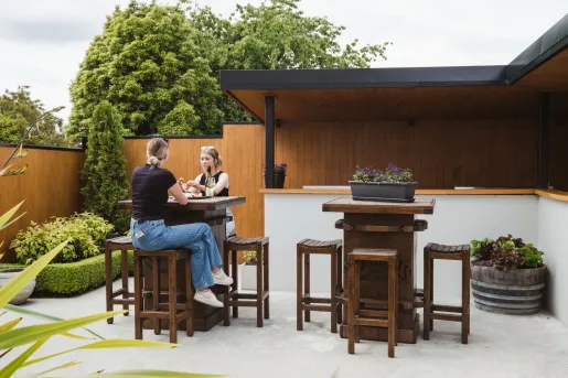 Outdoor patio with two people sitting on tall, wooden stools