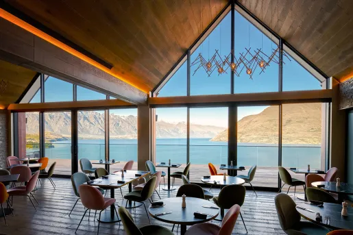 Indoor dining hall with large glass walls, looking out to tall mountains and a lake