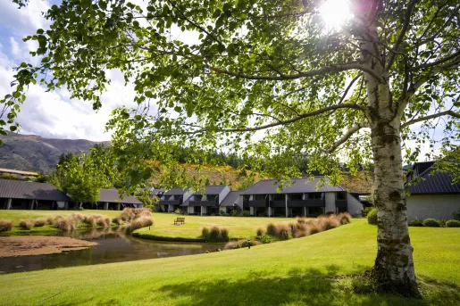 Exterior view of hotel buildings with large balconies, with a grass field and small lake in front
