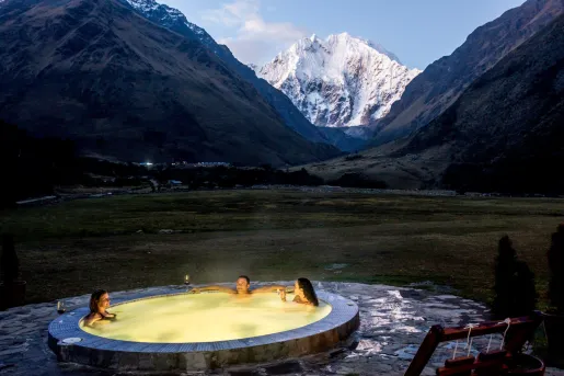 Outdoor hot tub with an illuminated yellow light, with snow capped mountains in the background