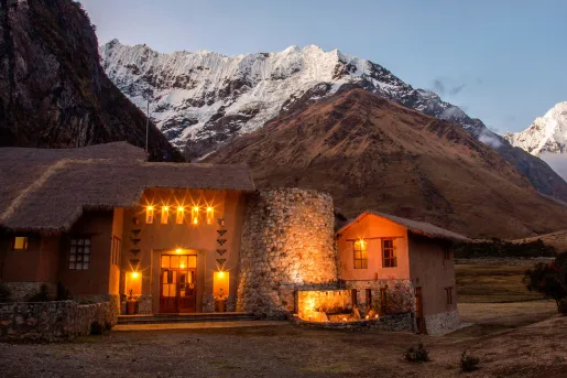 Stone building with straw roofing, with illuminated orange lights and snow-capped mountains in the backgroun