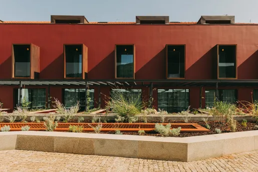 Exterior view of a red building with large windows and a small plant enclosure in front