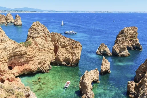 A boat navigating through large cliffs at the edge of the ocean