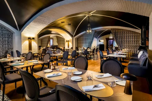 Restaurant dining hall with black cushioned chairs and large marble dining tables