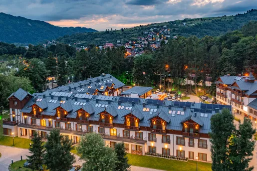 Exterior view of illuminated hotel building with wooden balconies and a forest in the background