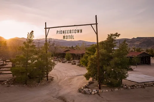 Dirt road leading to a large motel complex with a wooden sign saying "Pioneertown Motel"
