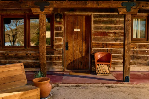 Exterior view of wooden lodge room with a leather chair and wooden bench in front