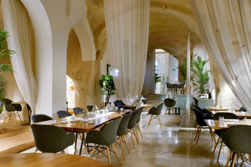 Indoor dining hall with long, rectangular tables and cushioned, gray chairs
