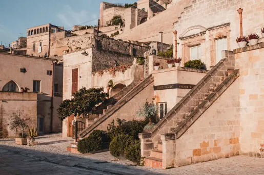 Exterior view of stone hotel building with 2 small staircases, bushes and small trees