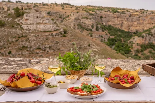 Table on the edge of a cliff with plates of toast and tomatoes, and two glasses of wine
