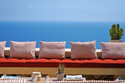 Balcony with cushioned bench with striped pillows, with views of the ocean in the distance