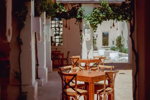 Outdoor patio with wooden tables and chairs, with large, white stone pillars