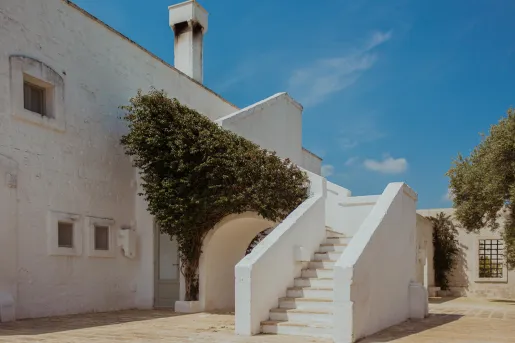 White, stone building with a staircase and bushy tree