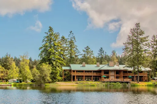 Exterior view of cabin-style building surrounded by trees and a lake in front
