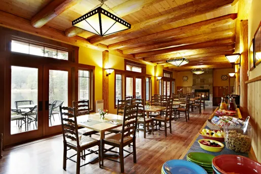 Cabin dining hall with wooden tables and chairs, with breakfast foods along the walls