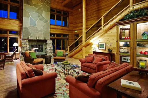 Cabin main room with cushioned, red sofas and a stone fireplace in front