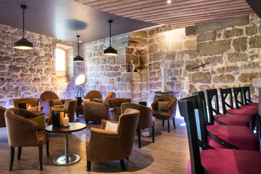 Tavern with cushioned chairs and circular tables, with stone walls