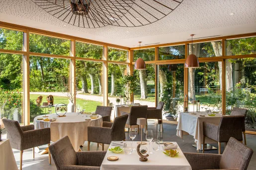 Dining room with cushioned chairs and white tables, in a room with large windows