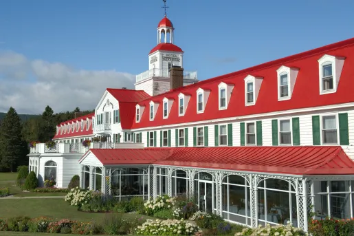 Exterior view of long red and white hotel building with bushes and a garden in front