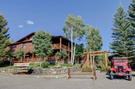 Exterior view of large cabin building with tall trees and a stone fence