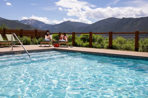 Two women sitting in front of an outdoor pool, with large mountains in the distance