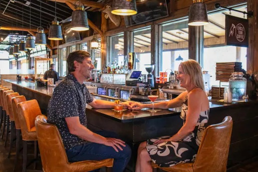 Man and woman smiling and holding hands while sitting at a bar
