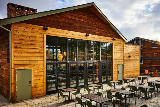 Exterior view of wooden cabin building with large glass doors and dining tables outside