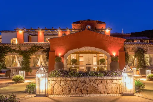 Exterior view of hotel building with stone archways and flowers in potted plants