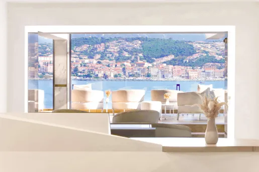 Cushioned white chairs on an outdoor patio looking out towards a large lake a distant town