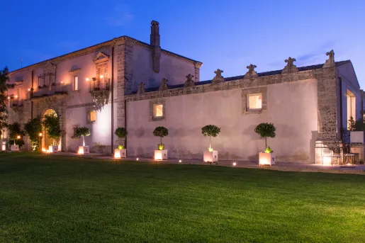 Castle-like building, surrounded by trimmed trees and a large grass field in front