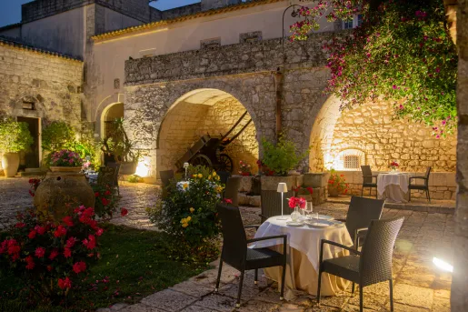 Outdoor patio and garden, with a stone building in the background and a dining table with black chairs