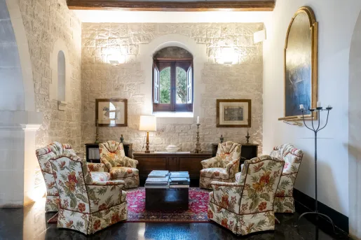 Seating area in a white, stone room, with cushioned chairs with flower patterns around a coffee table