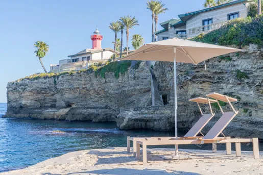 Two reclining chairs under an umbrella on the sand, on a beach