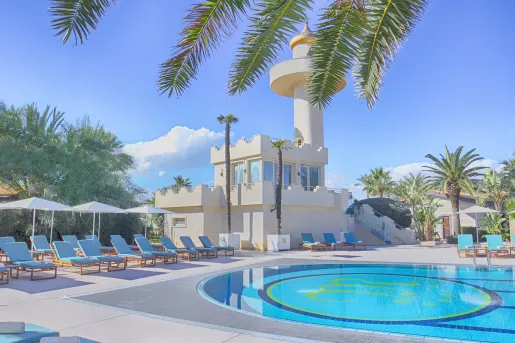Exterior view of white building and an outdoor pool, surrounded by white chairs