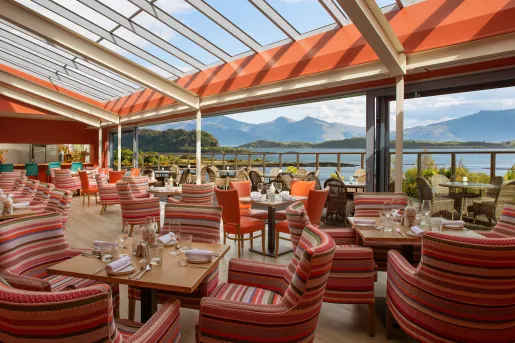 Outdoor dining area of a restaurant with striped red, cushioned chairs and square dining tables