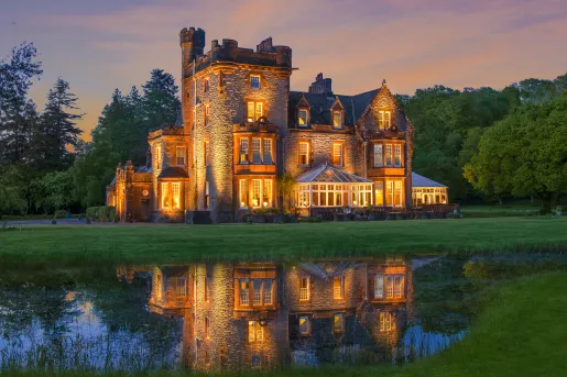 Illuminated, castle-like hotel building with a large grass field in front