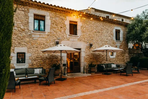 Exterior view of stone building with gray chairs and umbrellas in front