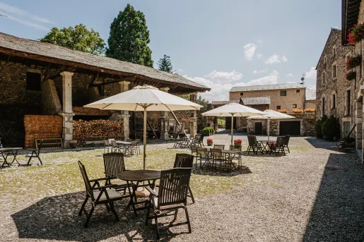 Outdoor area with dining tables covered with umbrellas, and stone buildings surrounding