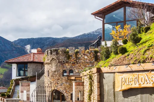Exterior view of stone buildings, with a staircase on the left and a statue on the top floor